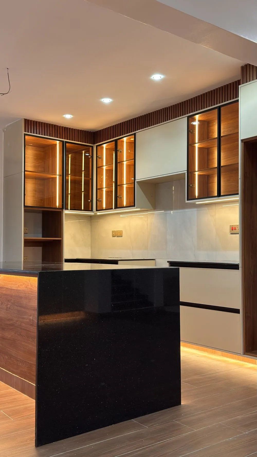 Finished kitchen in Cheptais with lit glass wall cabinets and a black stone waterfall island