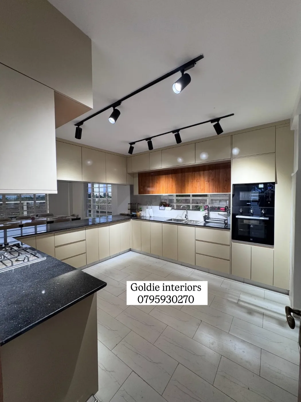 Cream handleless kitchen with a dark worktop, black track lights, a timber-toned wall cabinet run and a built-in oven and microwave