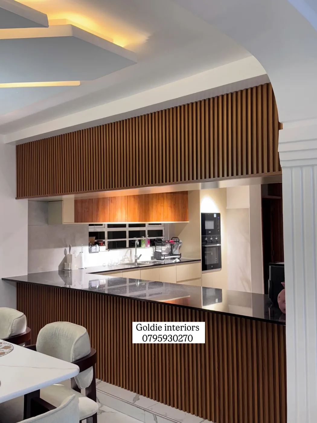Timber-slat bar front and upper screen between the dining area and kitchen, with a lit gypsum ceiling and an arched opening