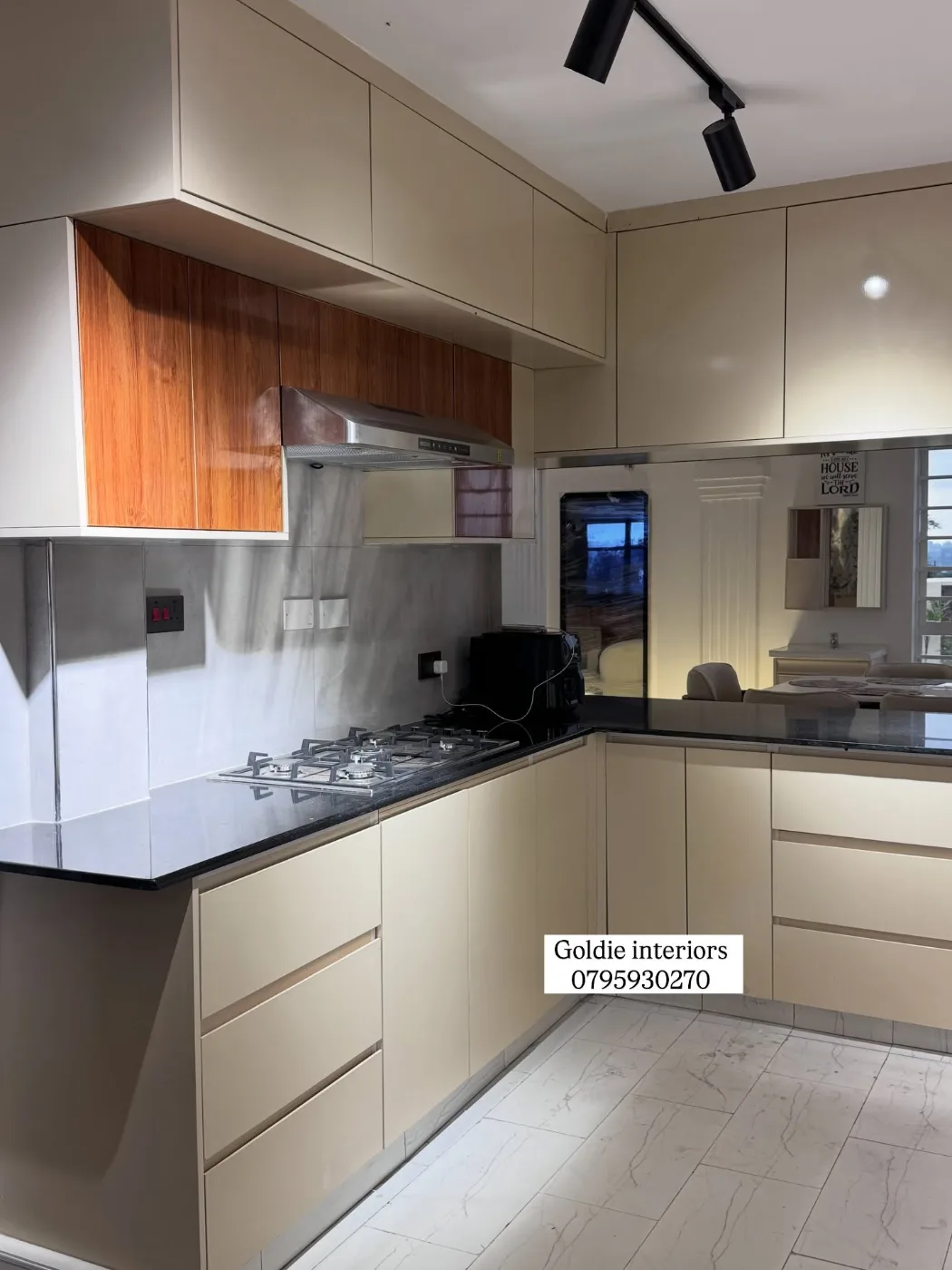Corner of the kitchen with cream drawers and cupboards, a dark worktop, gas hob, extractor, timber-toned wall units and a mirrored splashback