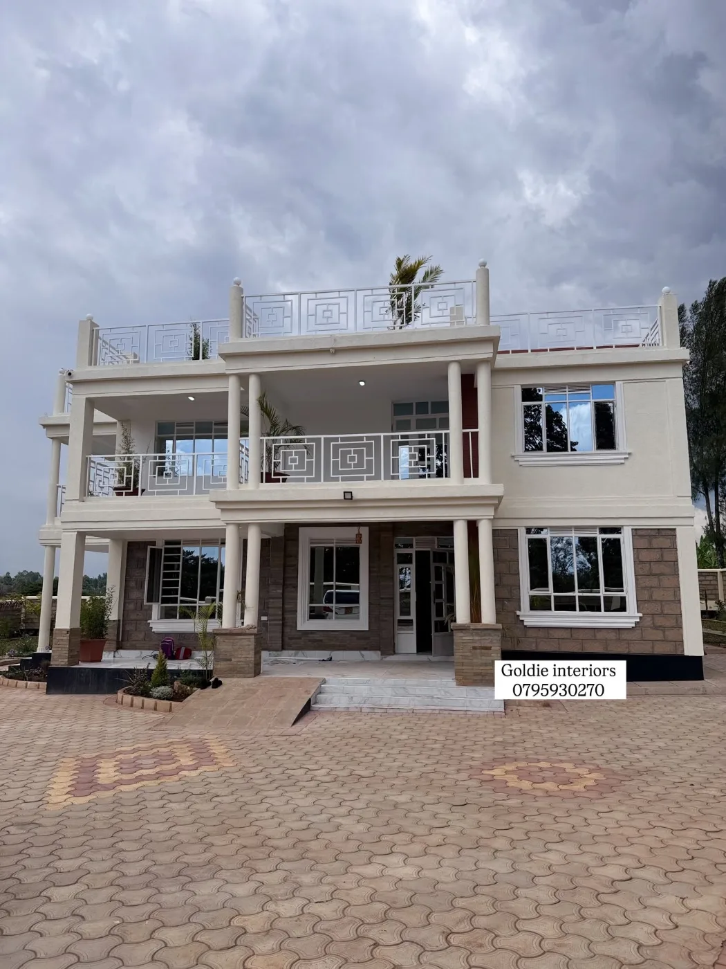 Front of the two-storey home with white columns, balconies with patterned white balustrades and a paved driveway