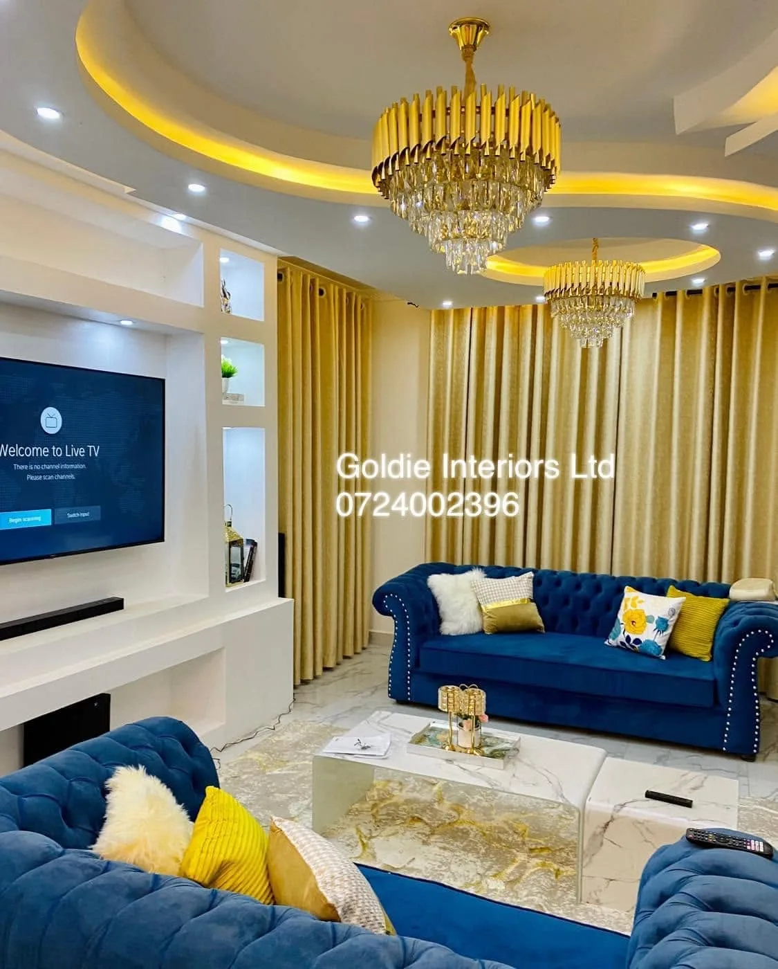 Blue Chesterfield sofa, gold chandelier, TV wall and a layered ceiling with warm LED lighting in the living room