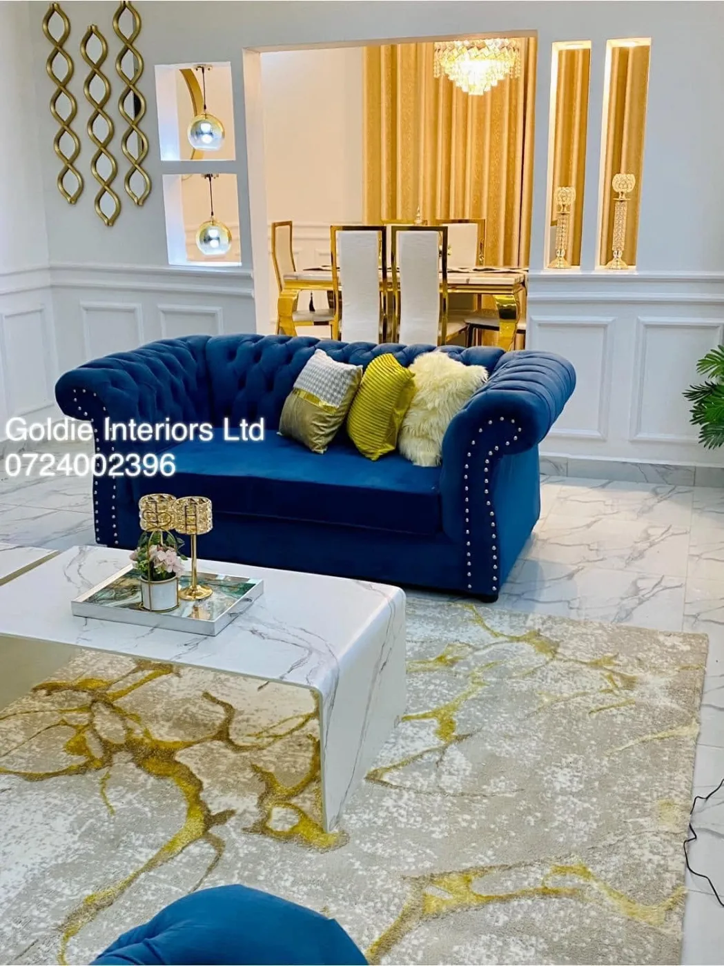 Blue studded sofa with mustard cushions on a gold-veined rug, with wainscoting and a gold-curtained dining area behind