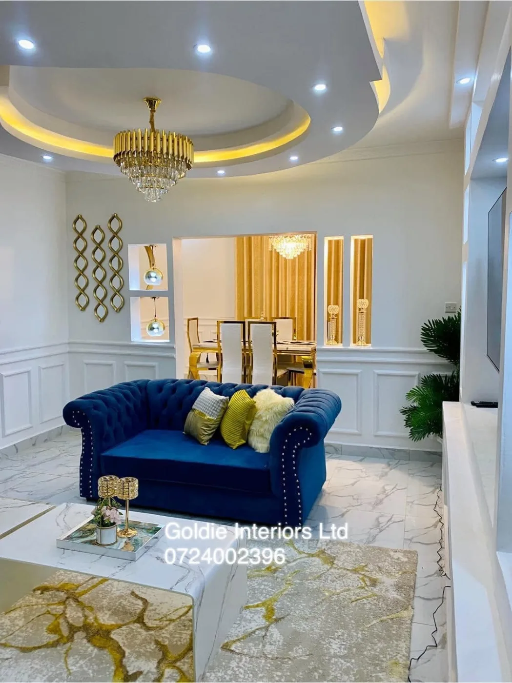 Living room seen across a marble-effect coffee table toward the blue sofa, wall panelling and diamond-shaped mirrors