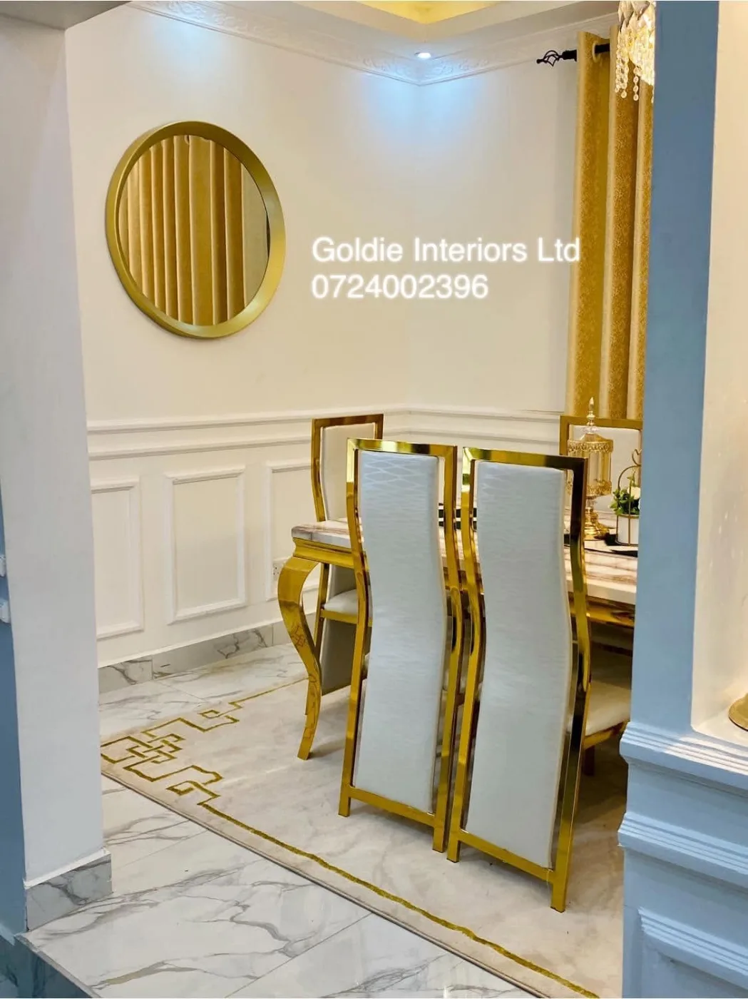 Dining corner with a round gold mirror, white wainscoting and gold-framed white chairs