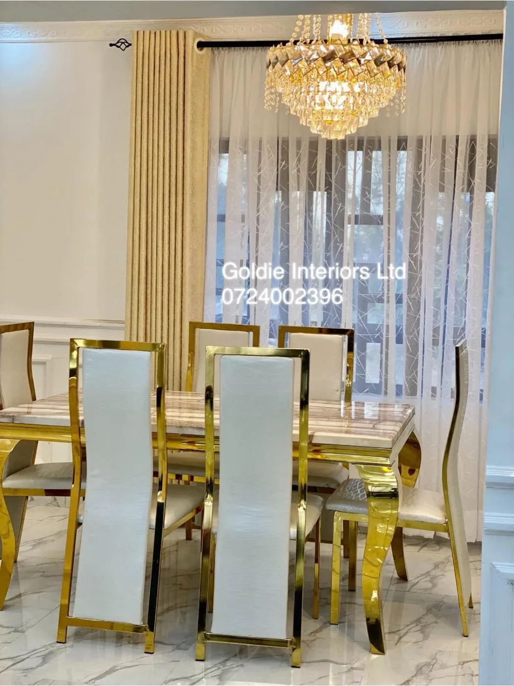 Dining table with gold-framed ivory chairs under a crystal chandelier, with sheer and gold curtains