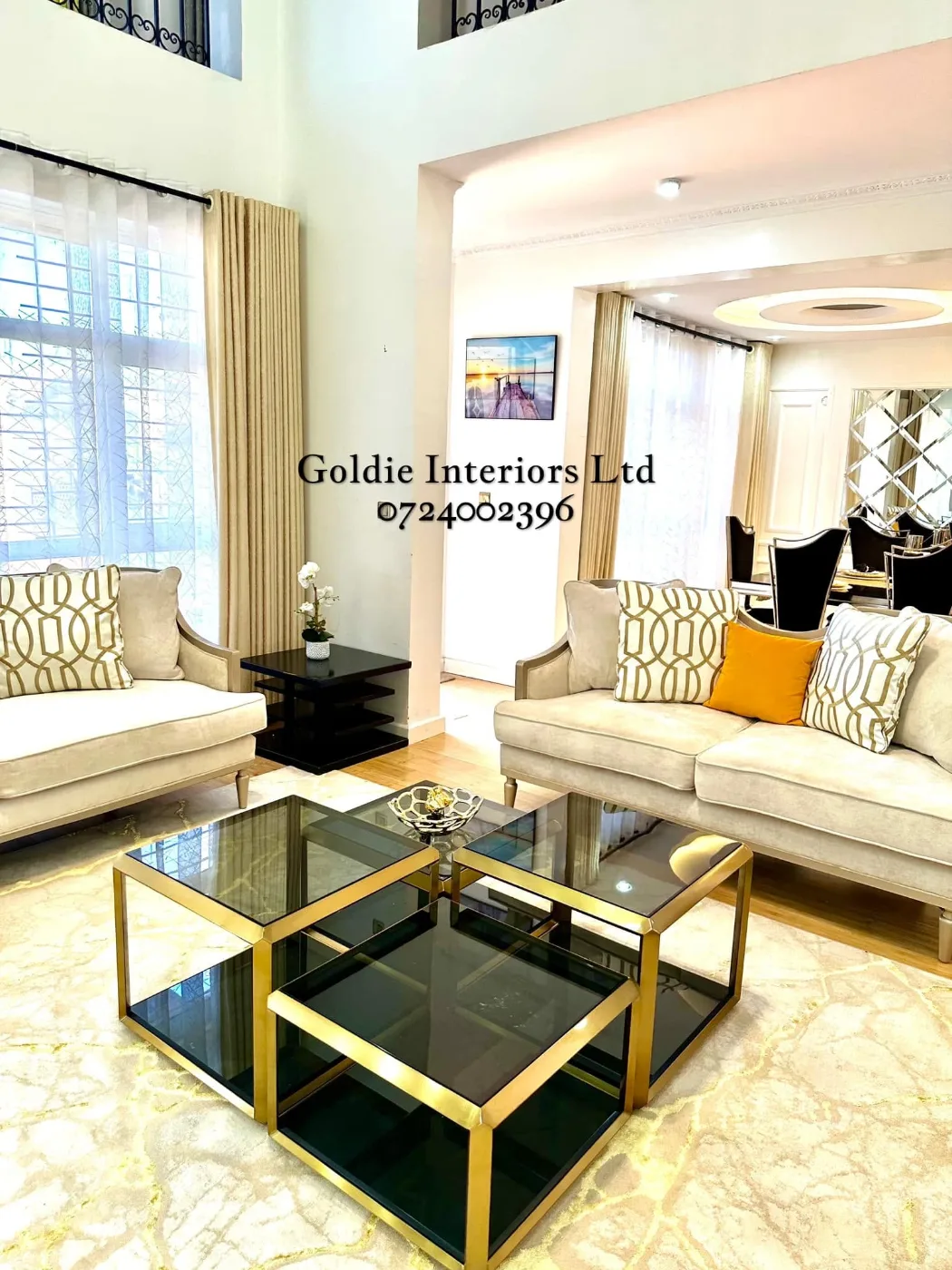 Living room with cream sofas and patterned cushions, gold-framed black glass coffee tables on a cream-and-gold rug, tall cream curtains with sheers and the dining room beyond