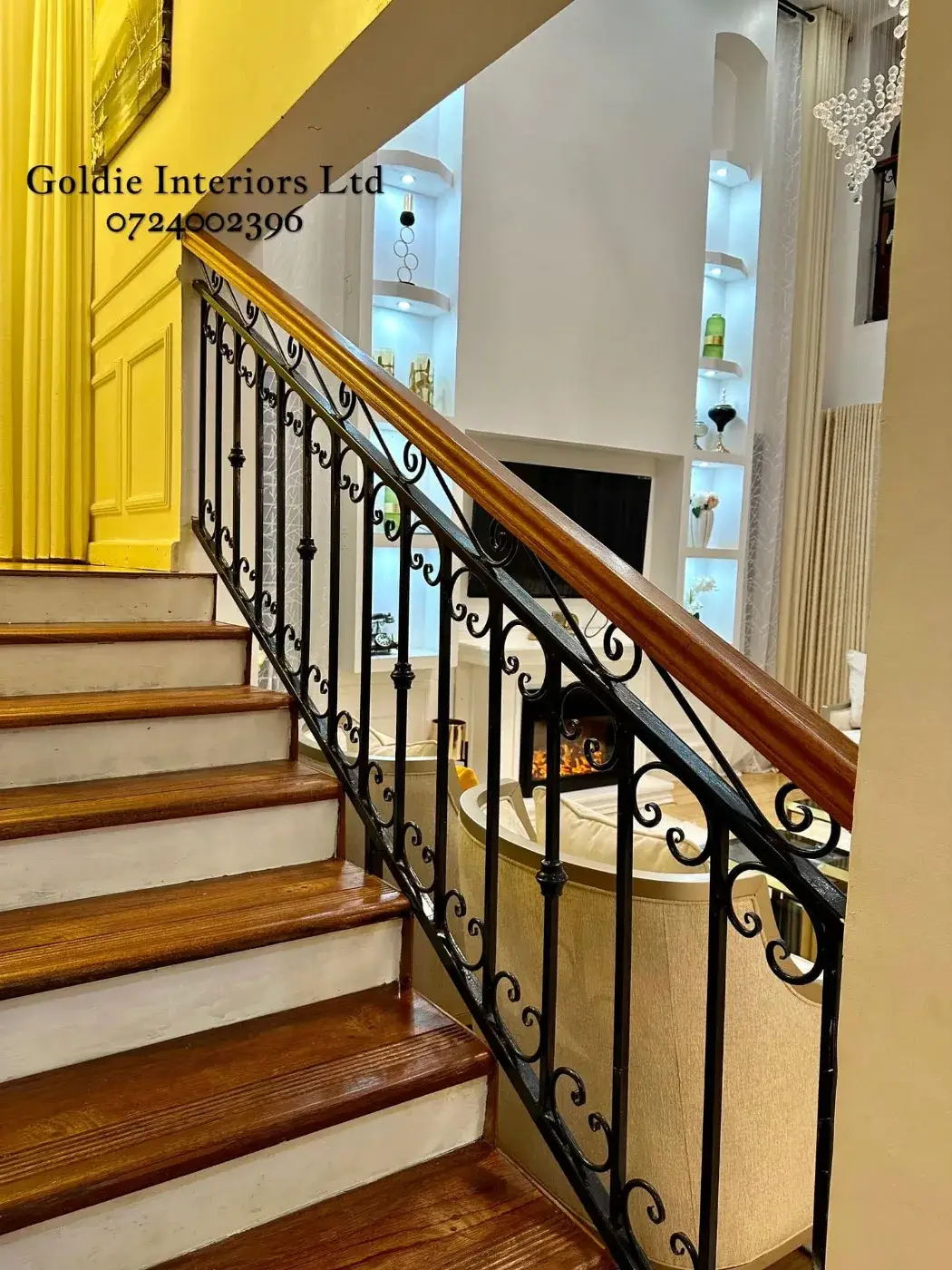Wrought-iron staircase with a timber handrail and timber steps, looking across to the lit niches and fireplace in the living room