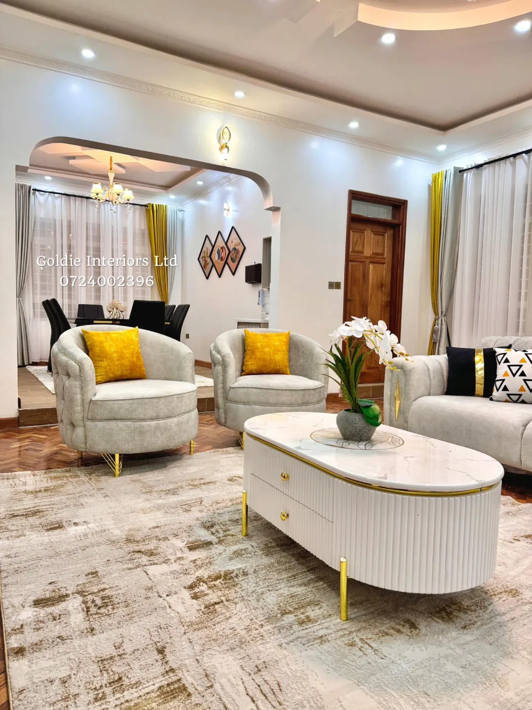 Living room with pale grey swivel armchairs, a fluted white coffee table and a sofa, with the dining area through an arch