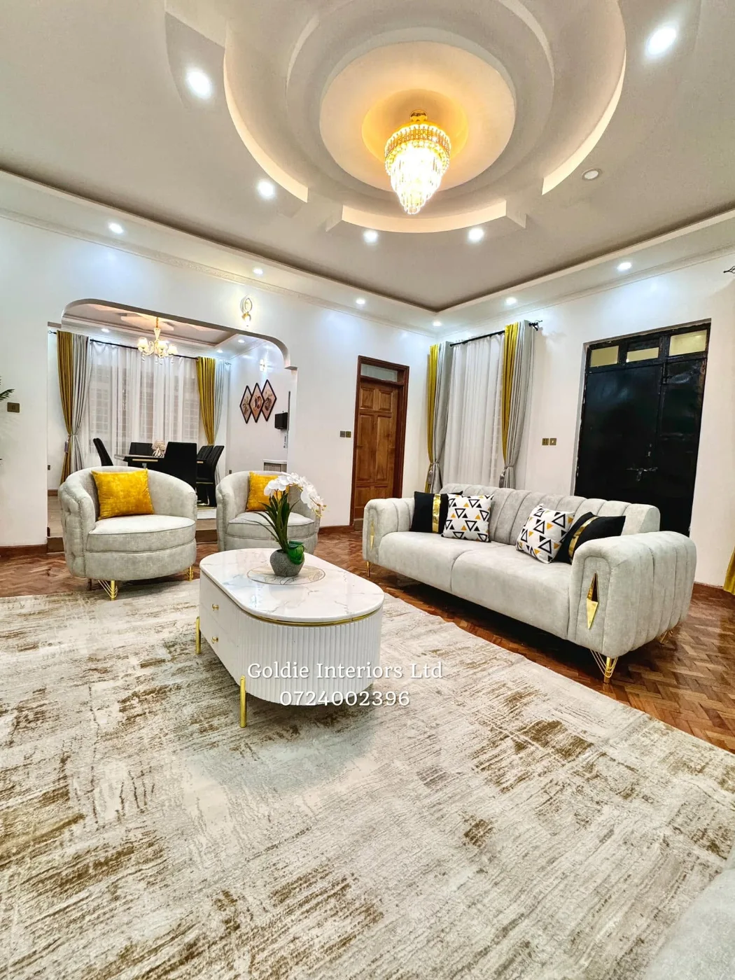 Living room under a circular gypsum ceiling with a chandelier, grey sofas on a soft gold-and-cream rug