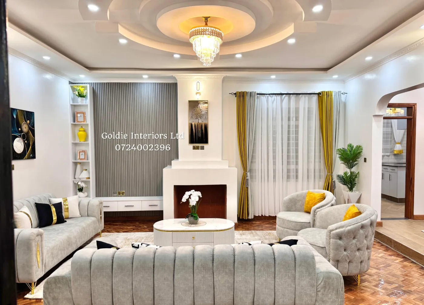 Wide view of the living room with a slatted feature wall, white surround and a grey sofa and tub chairs