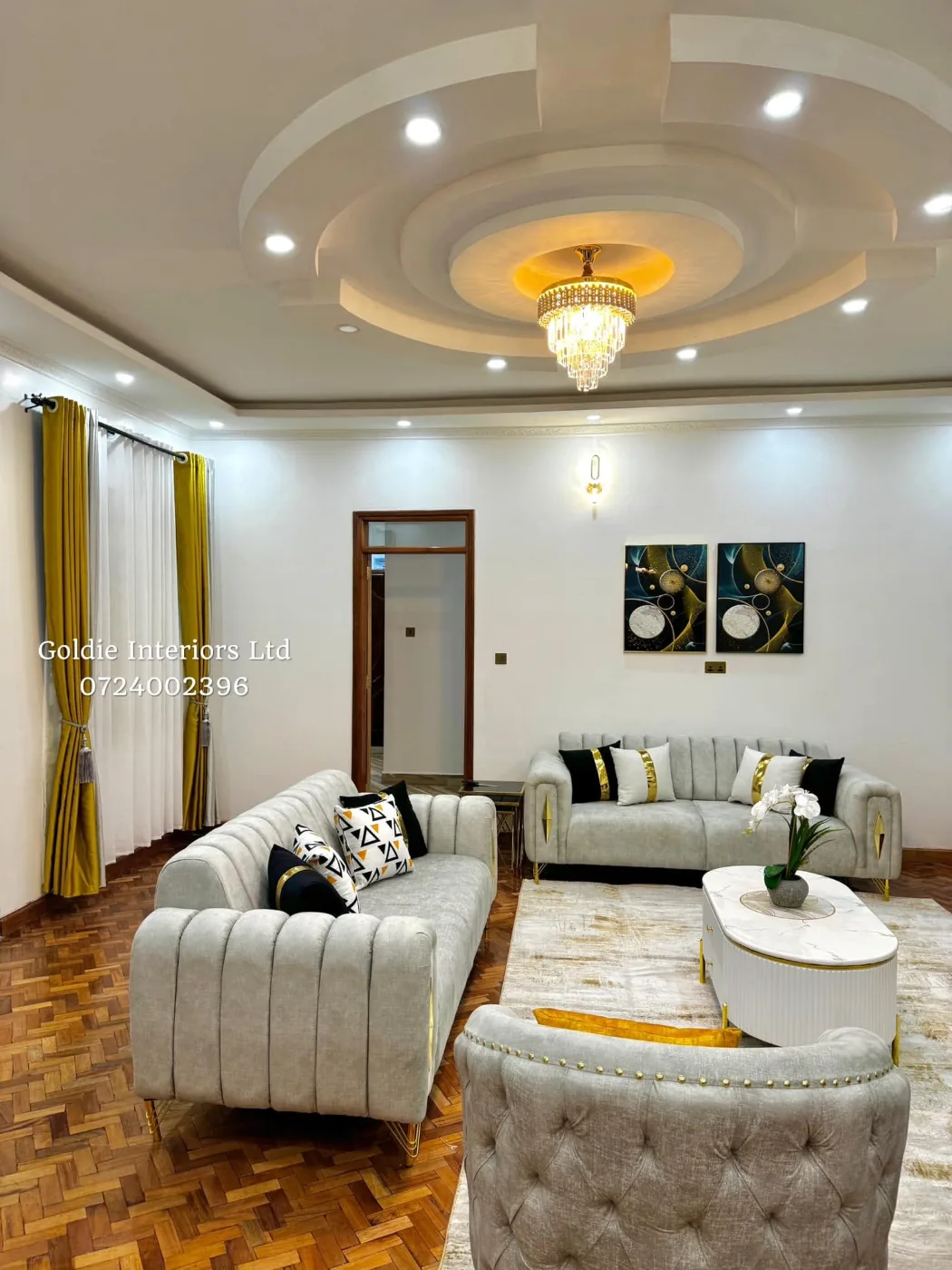 Sitting area with grey sofas, a white oval coffee table and gold-and-black wall art on parquet flooring