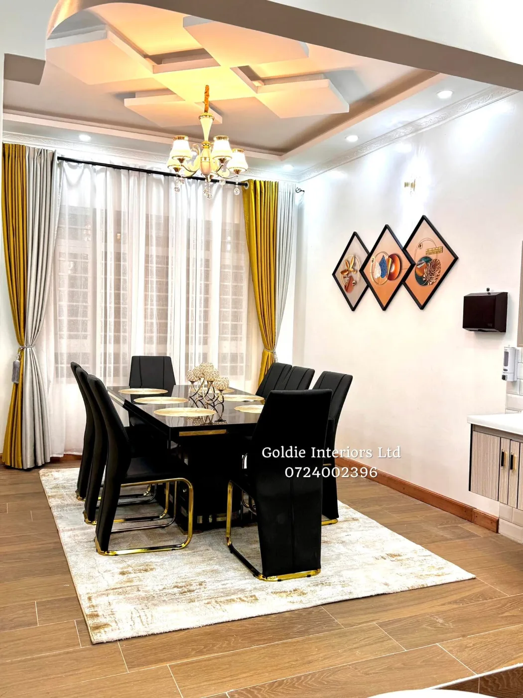 Dining table with black chairs with gold trim on a cream rug over a wood-look floor, with diamond wall art