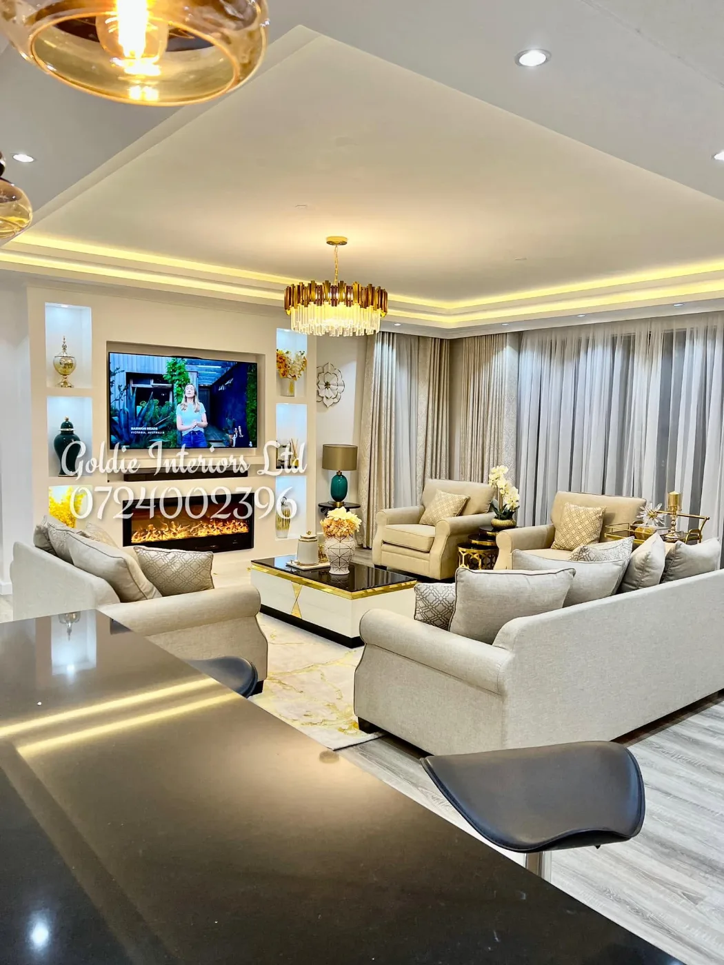 Living area with cream sofas and armchairs and a TV above an electric fireplace, seen over the black kitchen counter