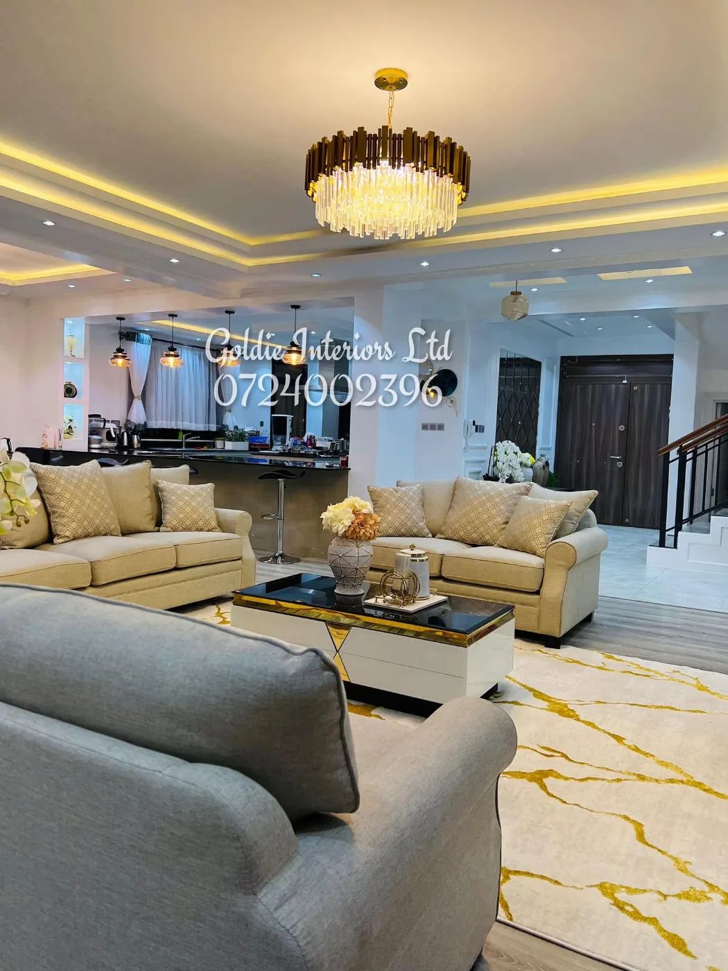 Open-plan living and kitchen with a crystal chandelier, cream sofas and a gold-veined rug