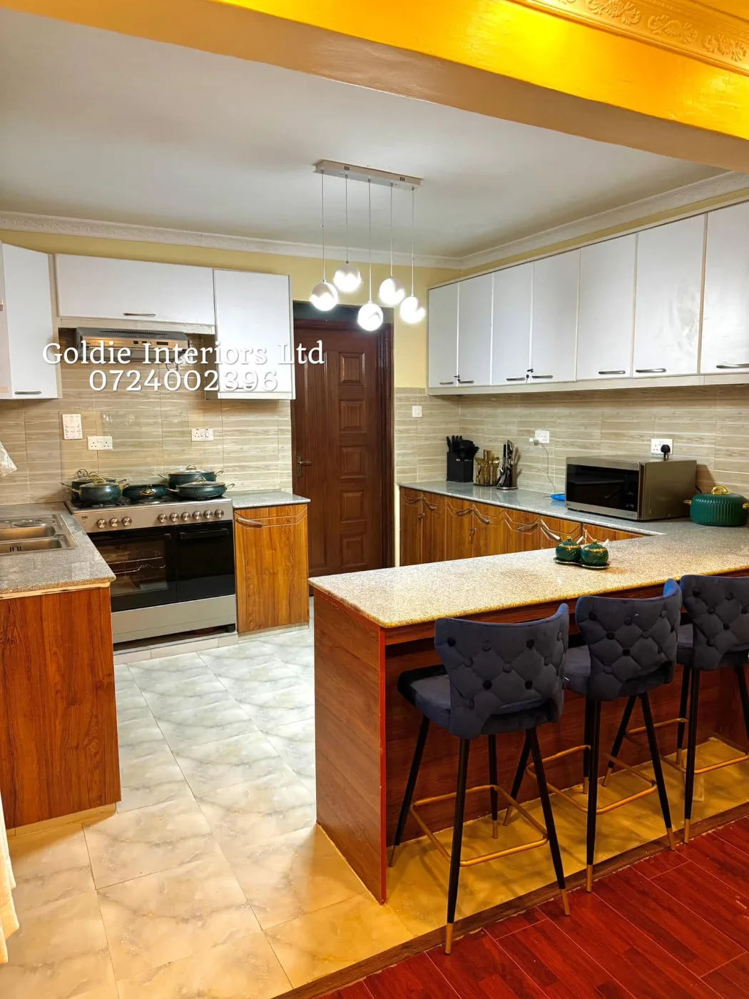 Kitchen with white wall cabinets, wood-look base units, a granite-effect worktop, a five-light pendant and navy tufted counter stools at the breakfast bar